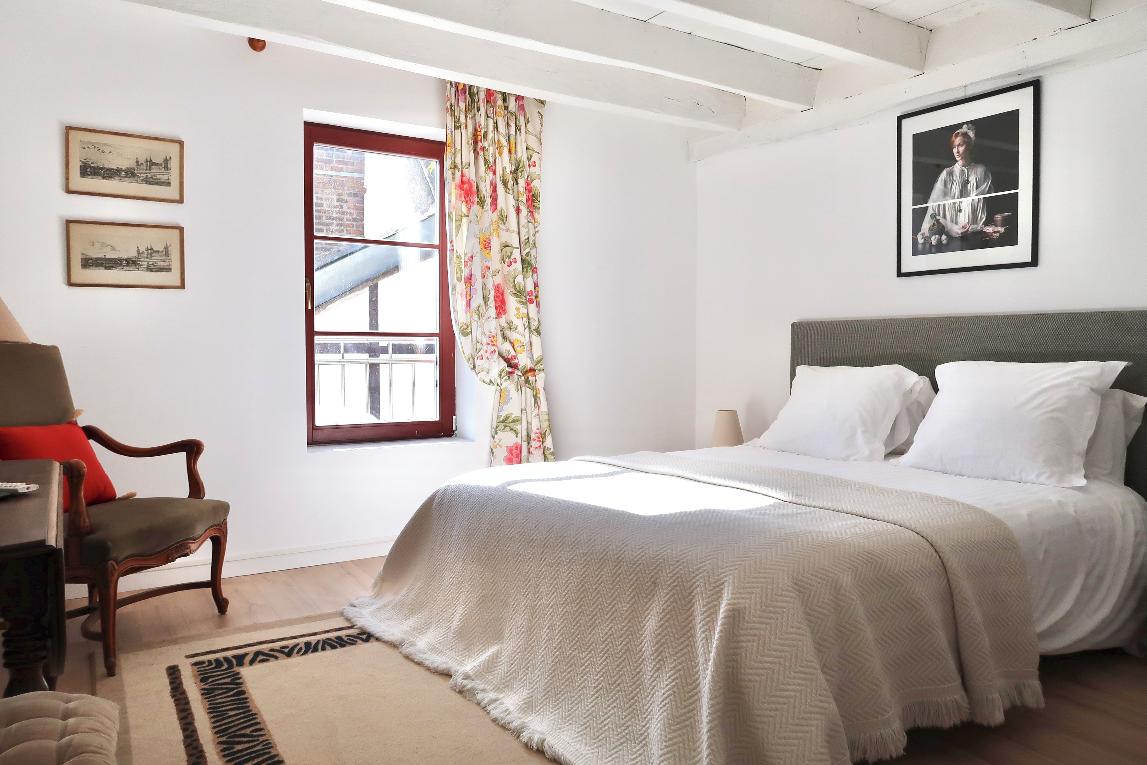 Een slaapkamer met een bed, een stoel, een bureau en een raam met gordijnen.