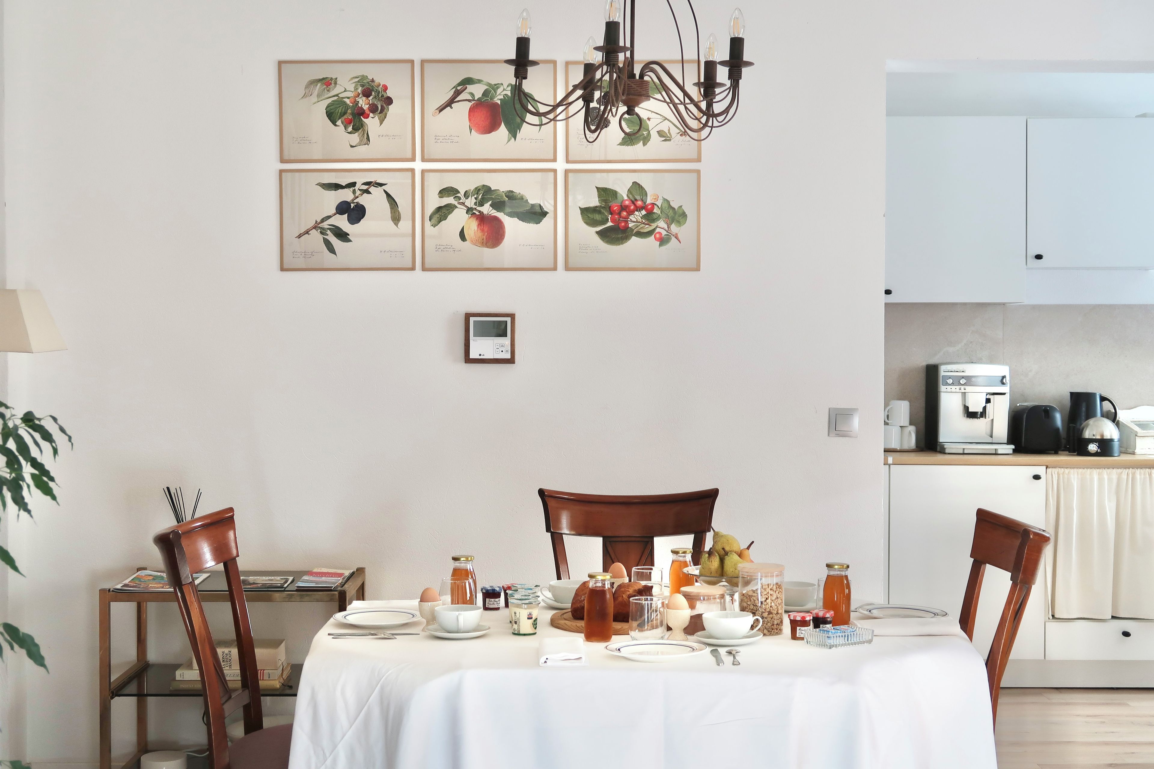 A dining area with a table set for four, surrounded by chairs, with a kitchen in the background.