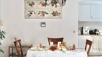 A dining area with a table set for four, surrounded by chairs, with a kitchen in the background.