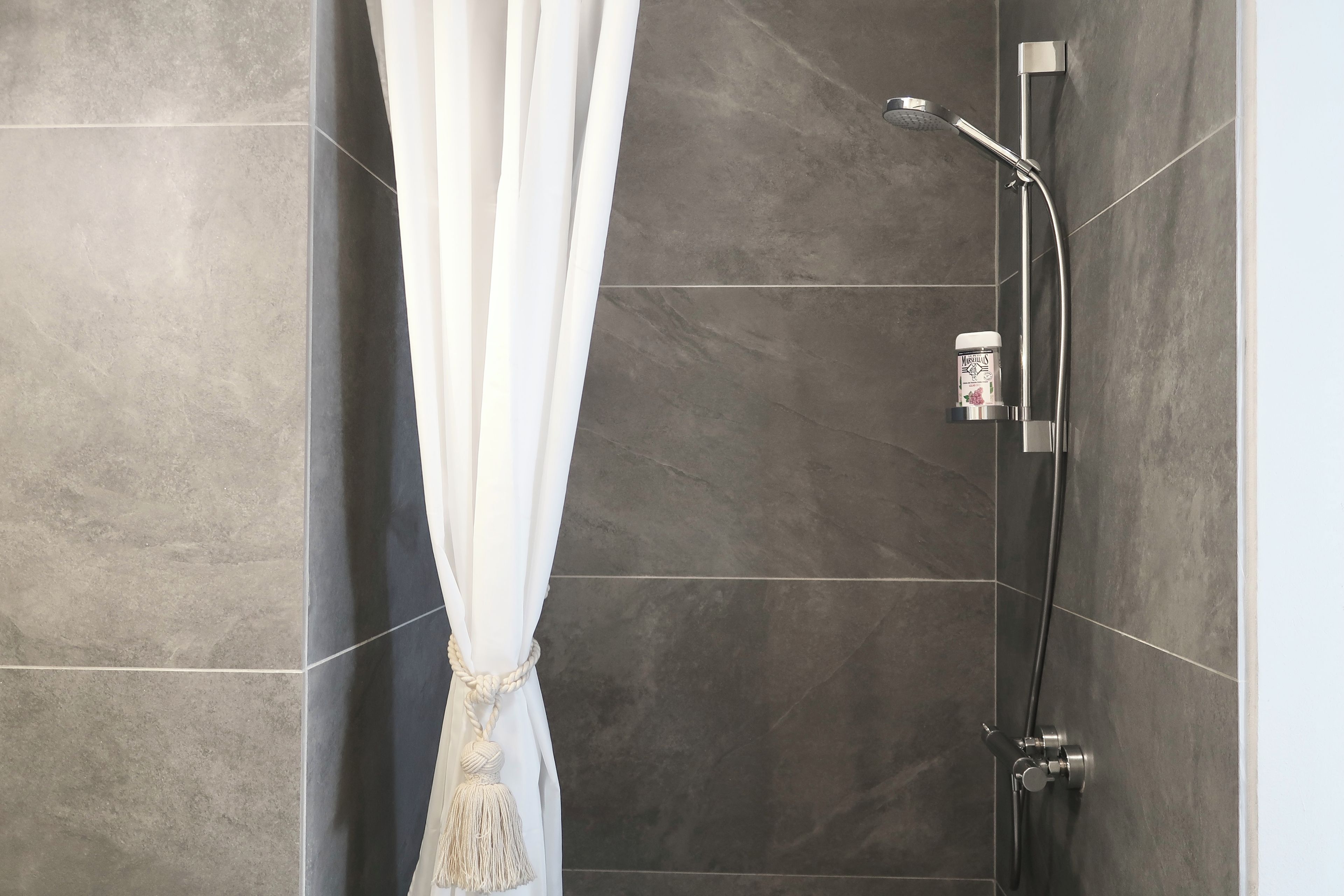 Une douche équipée d’un pommeau de douche à main et d’un panneau de commande fixé au mur.