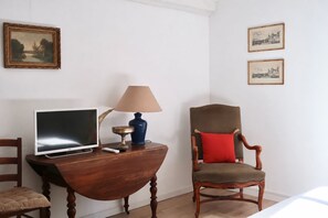 Een hotelkamer met een houten bureau, een televisie, een lamp, een stoel en twee ingelijste foto's aan de muur.