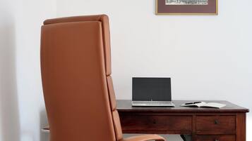 Una silla de cuero marrón, un escritorio de madera con una computadora portátil y un cuadro en la pared.