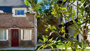A brick building with a red door, a window with shutters, and a small garden area with a gravel path. - La grange à grains (Château-Renard)
