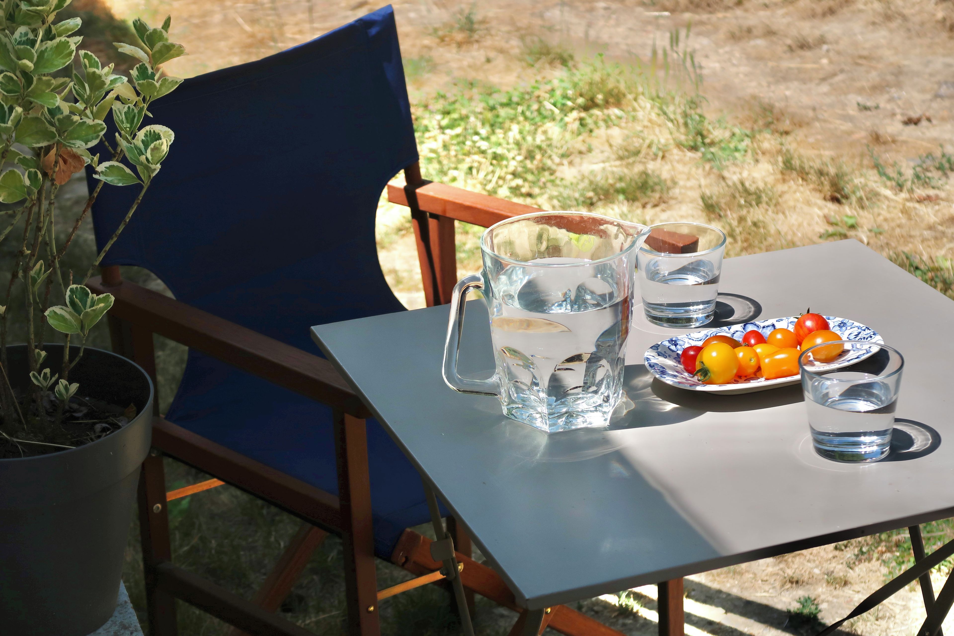 A table set outdoors with a pitcher, glasses, and a plate of tomatoes.