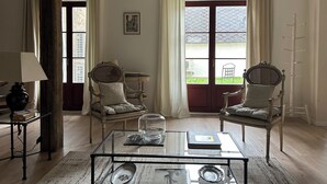 A room with two wicker chairs, a glass coffee table, a small table with a lamp, and a window with curtains. - La grange à grains (Château-Renard)