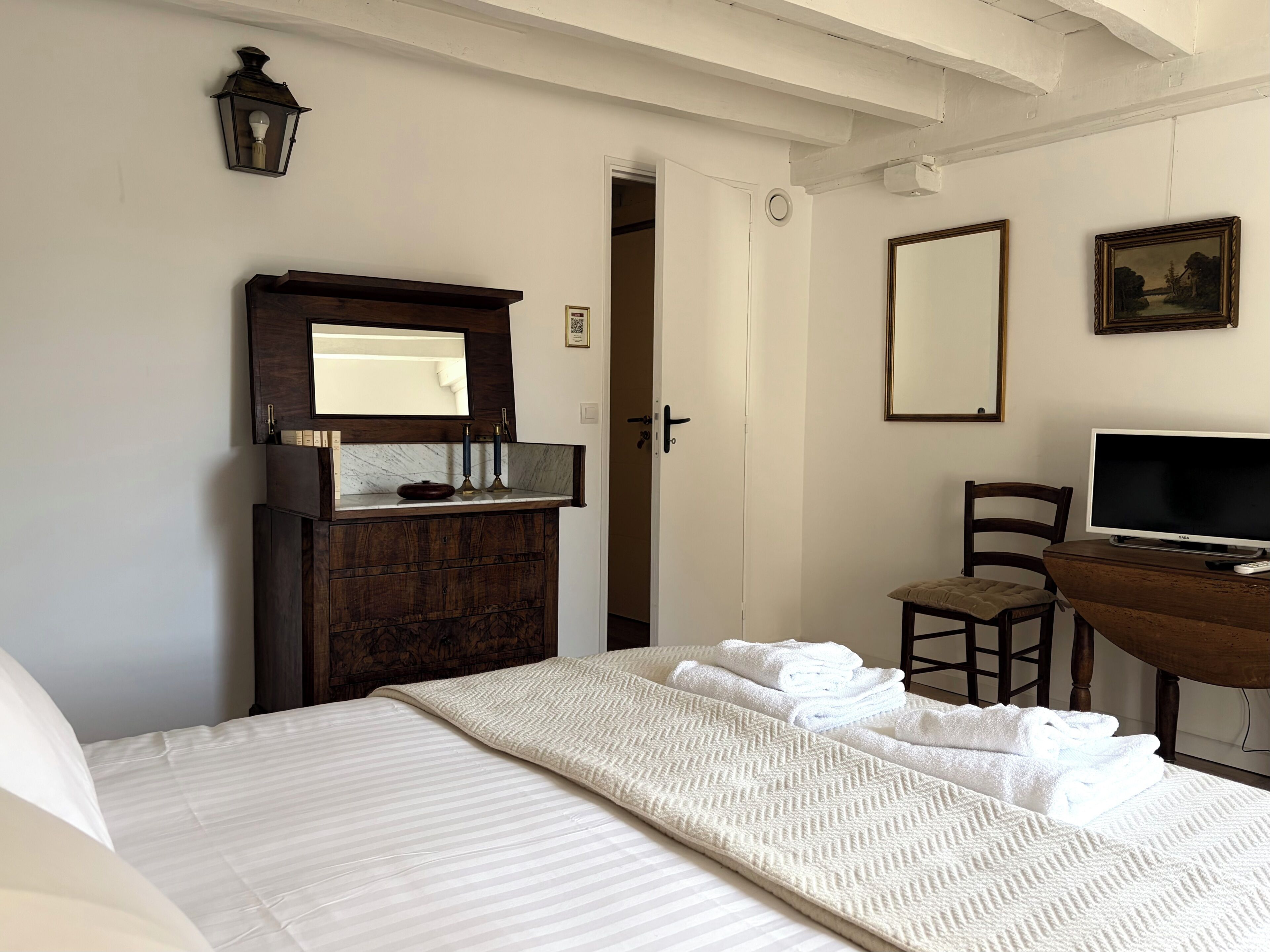 A bedroom with a bed, a dresser, a television, and a door leading to another room.