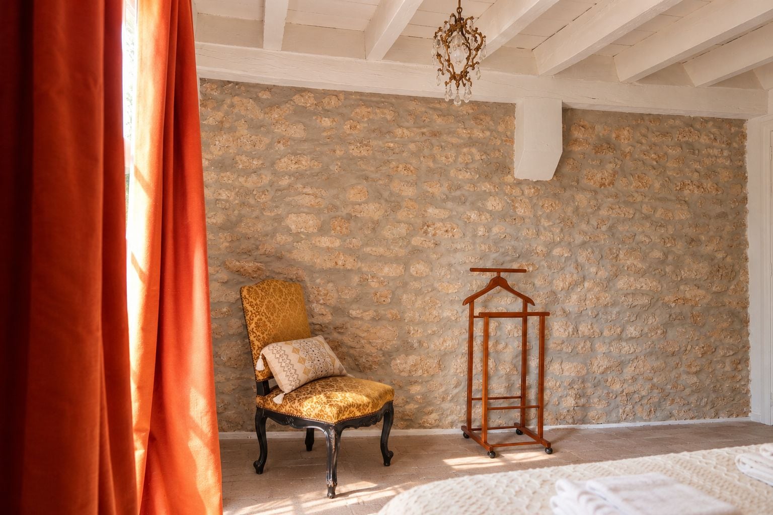 A room with a stone wall, a chair with a patterned cushion, a wooden hanger, and a hanging light fixture.