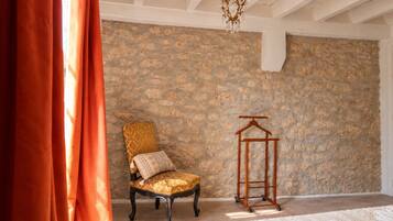 A room with a stone wall, a chair with a patterned cushion, a wooden hanger, and a hanging light fixture.