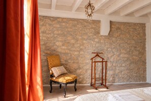 Une pièce avec un mur en pierre, une chaise avec un coussin à motifs, un cintre en bois et un luminaire suspendu.