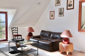 Un salon avec un canapé en cuir marron, deux lampes, un fauteuil et une table basse en verre.