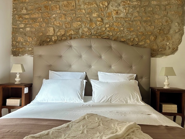 Una cama con cabecera capitonada, ropa de cama blanca y dos mesitas de noche con lámparas.