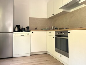 A compact kitchen with a dishwasher, oven, and a coffee maker on the countertop.