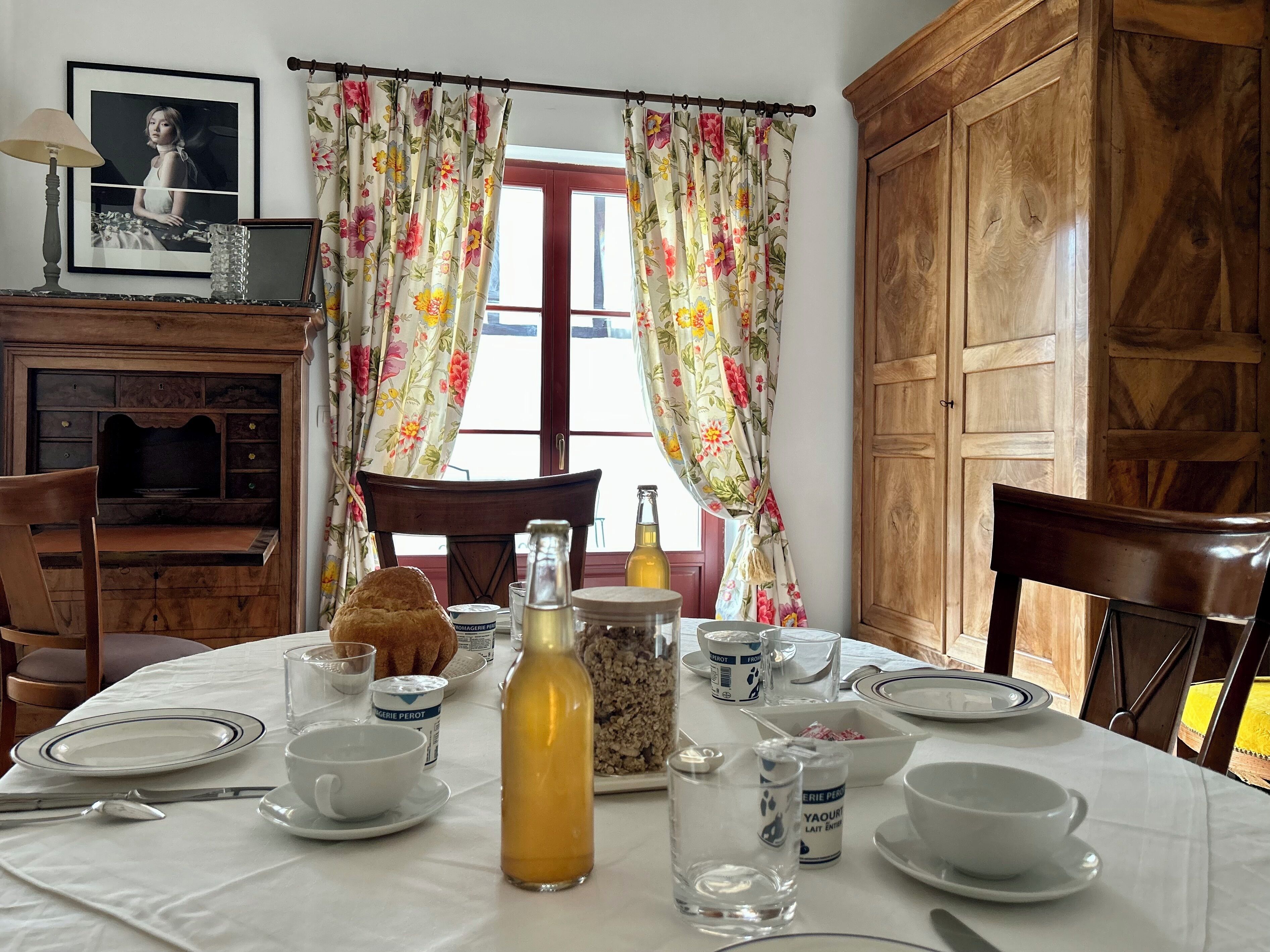 Comedor con una mesa dispuesta para dos personas, que incluye una botella de jugo, un vaso, platos y cubiertos. Se aprecia un armario de madera y un cuadro enmarcado al fondo.