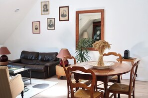 Una sala de estar con un sofá de cuero oscuro, una mesa de comedor de madera con sillas, un espejo grande y cuadros en la pared.