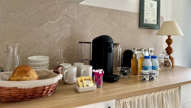 A kitchen counter with a coffee maker, mugs, a basket with bread, and various food items. - La grange à grains (Château-Renard)
