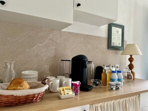 A kitchen counter with a coffee maker, mugs, a basket with bread, and various food items.