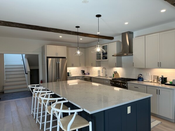 A modern kitchen with a large island, stainless steel appliances, pendant lighting, and a dark blue accent wall.