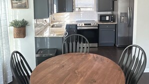 Una cocina moderna con armarios oscuros, un refrigerador de acero inoxidable, un microondas y una estufa. Hay una mesa de madera con cuatro sillas.