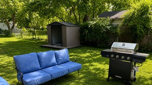 Un patio trasero con un sofá azul, una parrilla y un cobertizo.