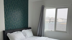 Cama bem arrumada com roupa de cama branca, cabeceira escura e parede com padrão geométrico.
