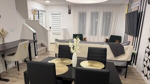 Uma sala de estar moderna com uma mesa de jantar, cadeiras pretas, um sofá e uma televisão.
