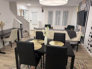 Ein modernes Wohnzimmer mit einem Esstisch, schwarzen Stühlen, einer Couch und einem Fernseher.