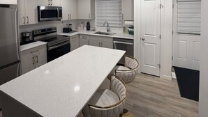 Uma cozinha moderna com armários brancos, eletrodomésticos de aço inoxidável, uma ilha central e um banqueta.