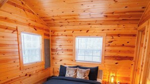 A cozy log cabin bedroom with a bed, two windows, a ceiling fan, and a nightstand.
