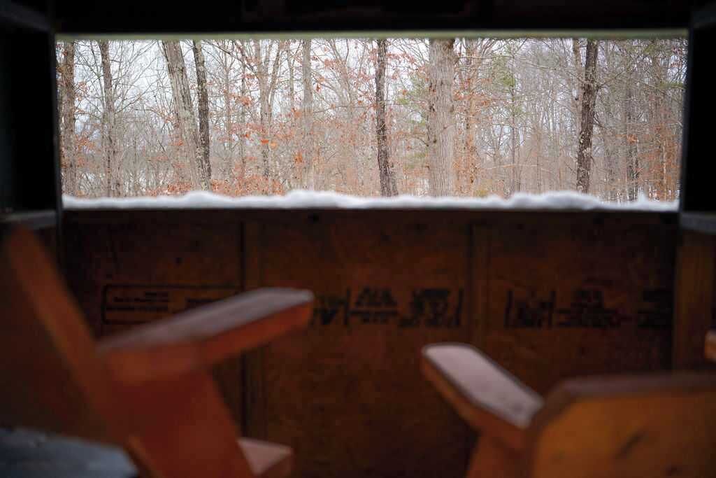 Ein Zimmer mit Fenster und Blick auf einen Wald, mit Holzwänden und einem Stuhl.