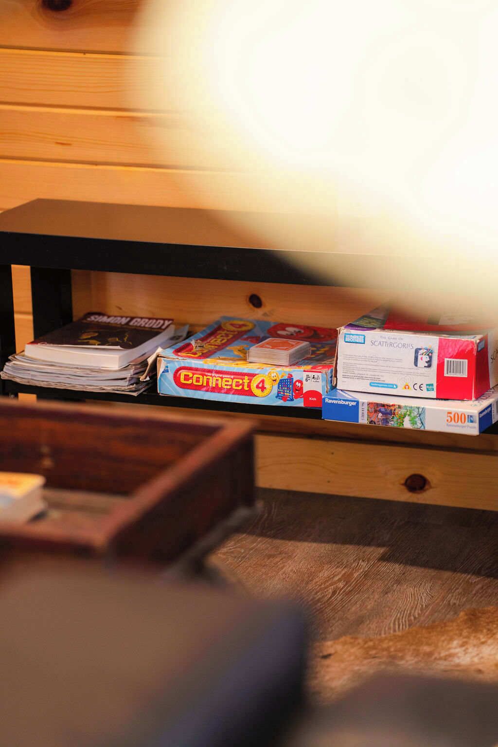 A wooden table with a stack of books, Connect 4 game boxes, and a Ravensburger puzzle box.