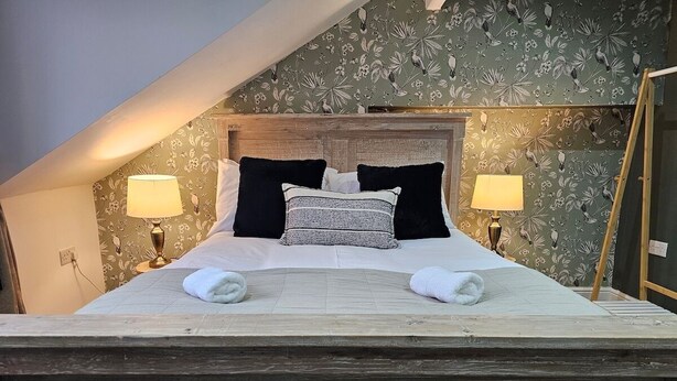 A bedroom with a wooden headboard, two bedside lamps, a bed with white linens, and a floral wallpaper pattern. - 10% Off Weekly Stay|Chatsworth Retreat|Sleeps 7 (North Yorkshire)