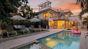 A modern house with a swimming pool, outdoor seating, and a well-lit interior. - Soleil Modern by Avantstay Design-forward Stay + Resort-style Pool + Hot Tub + Near the Beach (Fort Lauderdale)