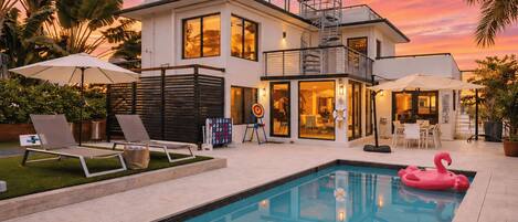 A modern two-story building with a swimming pool, outdoor seating, and a balcony.