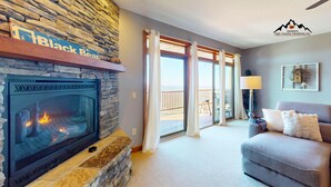 A living room with a stone fireplace, a balcony with curtains, and a grey sofa. - Reserve 27D • Big Skyline Views (Sugar Mountain)