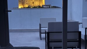 A modern living room with a sofa and chairs, a glass table, and a view of a historic castle illuminated at dusk. - House in Belalcazar overlooking the Castle (Belalcázar)