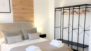 A neatly made bed with a beige bedspread, a wooden headboard, and a black metal wardrobe with wooden hangers. - House in Belalcazar overlooking the Castle (Belalcázar)