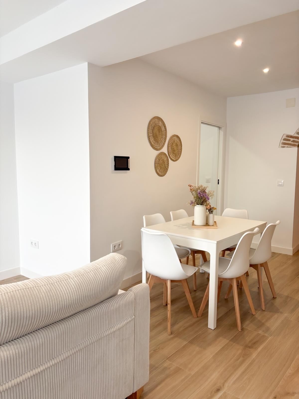 Een moderne eetruimte met een witte tafel, witte stoelen en een beige bank.