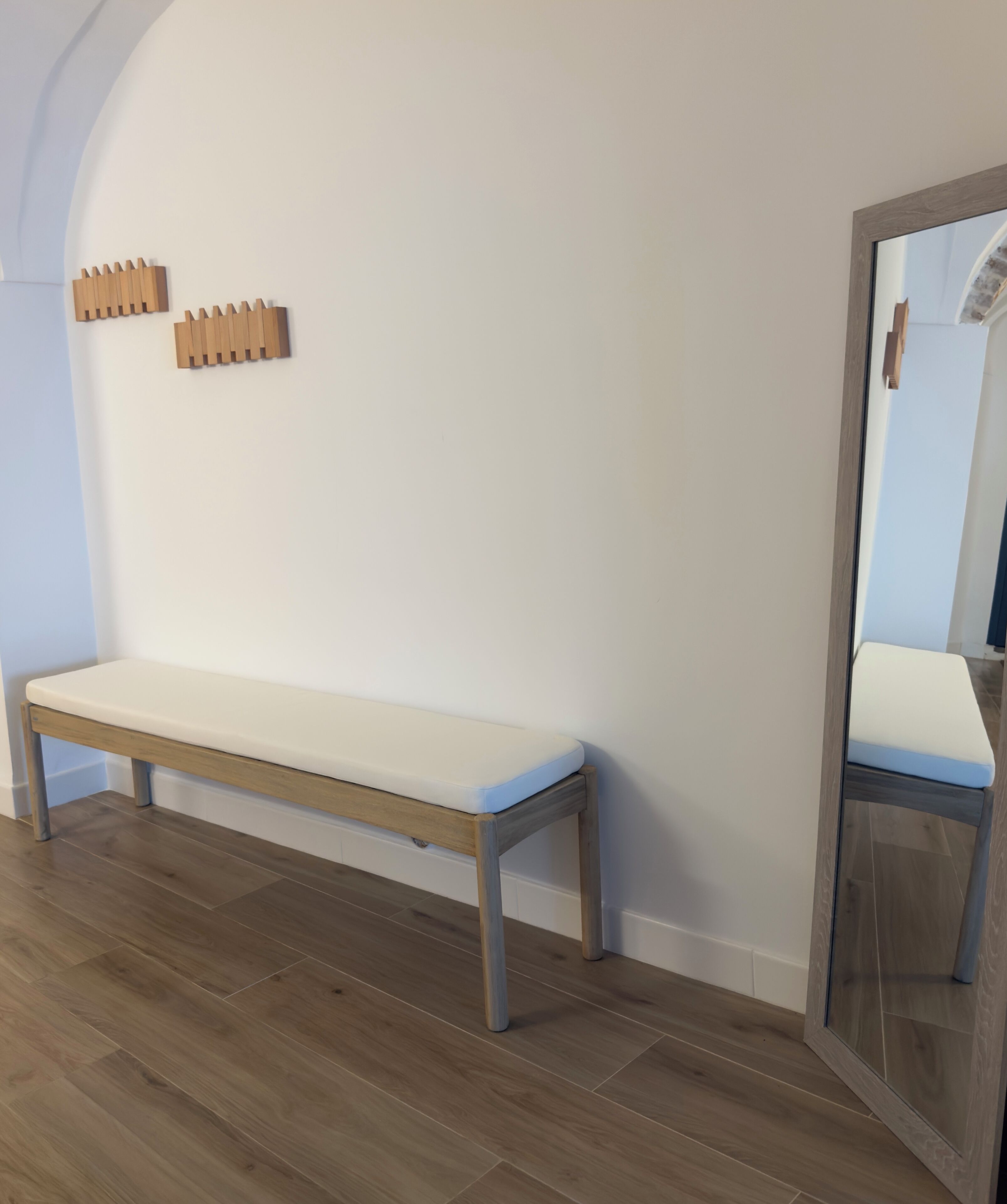 Un banco con cojín blanco, un adorno de pared de madera y un espejo con marco de madera.