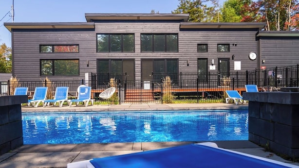A modern building with a swimming pool, lounge chairs, and a fenced area. - 2CH: Relaxation + Spa + Sauna + BBQ + Wi-Fi (Pont-Rouge)