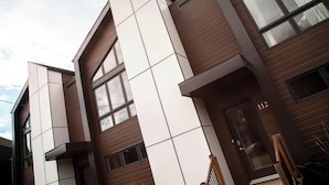 A modern building with a mix of wooden and white panels, large windows, and a visible door with the number 112. - 2CH: Relaxation + Spa + Sauna + BBQ + Wi-Fi (Pont-Rouge)