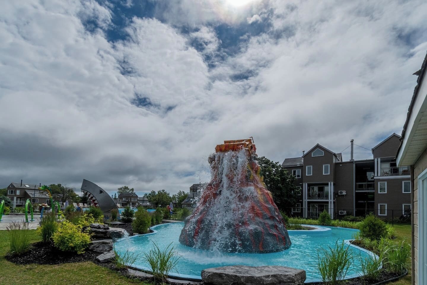 A water feature with a waterfall and a pool, surrounded by greenery and residential buildings.