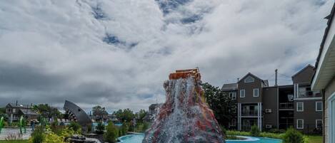 A water feature with a waterfall and a pool, surrounded by greenery and residential buildings.