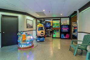 Corredor com jogos de fliperama, incluindo um carro de corrida e um jogo com personagens, e uma máquina de refrigerantes Pepsi.