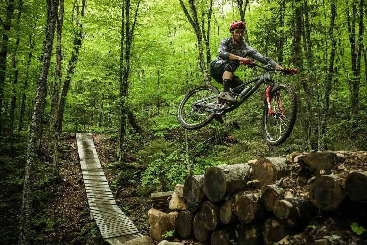 Uma pessoa andando de bicicleta de montanha sobre uma ponte de madeira em uma floresta.