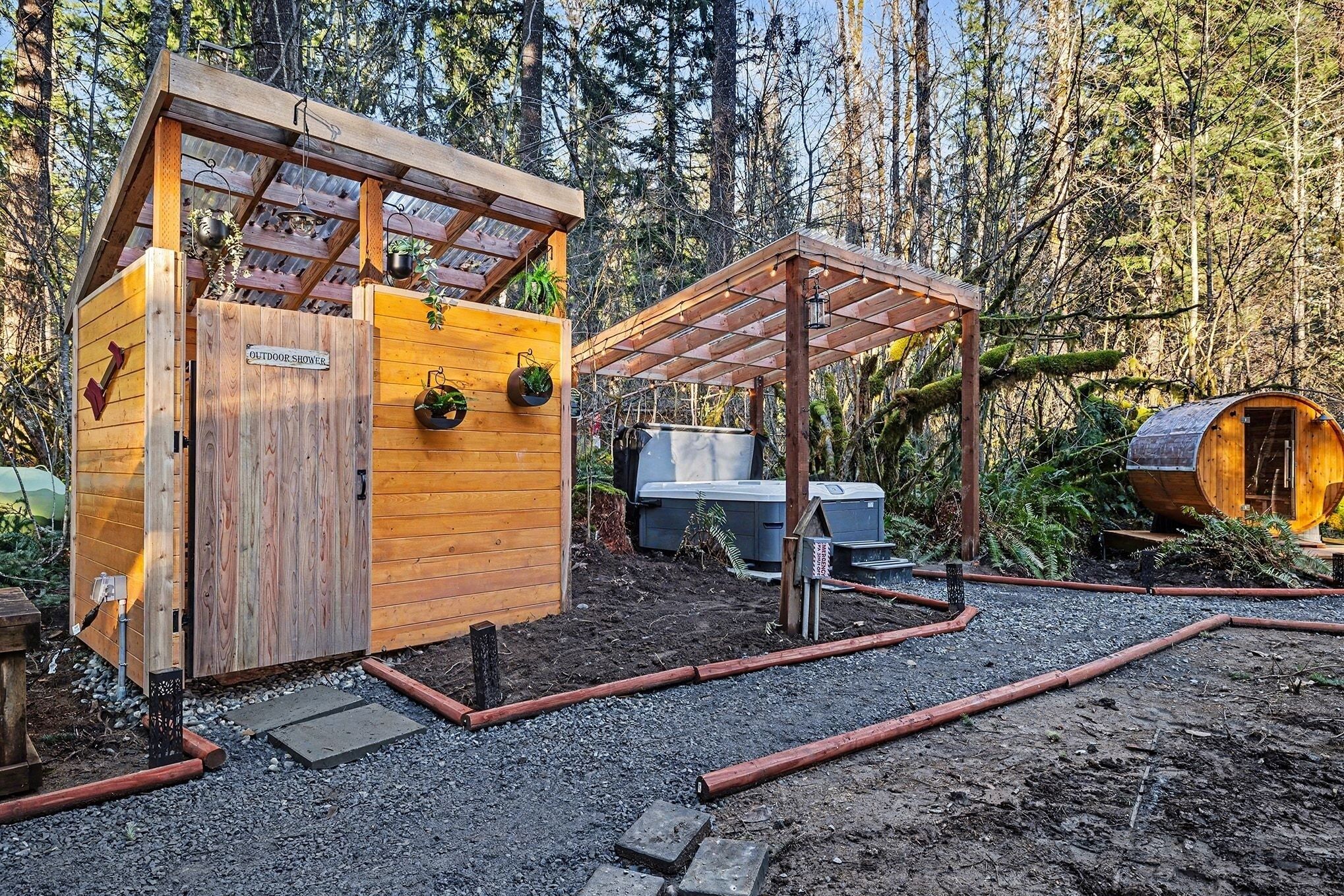 Een houten douchecabine buiten met een bordje, een overdekte zithoek en een sauna, gelegen in een bosrijk gebied.