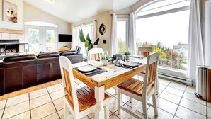 Ett modernt vardagsrum med en öppen spis, en matplats med ett träbord och stolar samt ett stort fönster med gardiner.