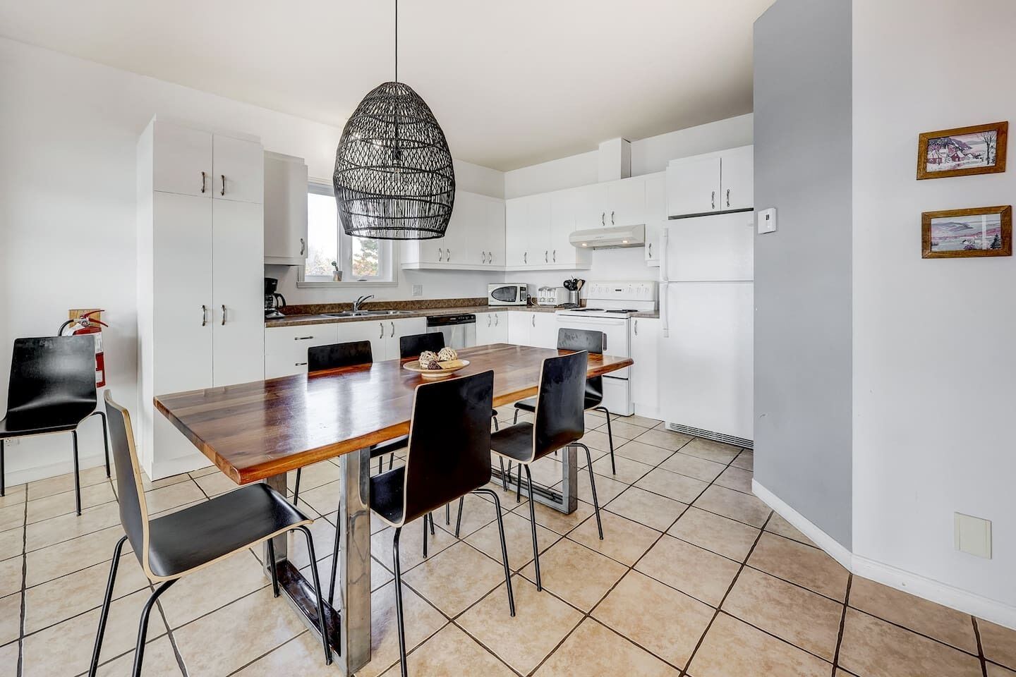 A modern kitchen with white cabinets, a wooden dining table, black chairs, and a hanging pendant light.