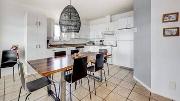 A modern kitchen with white cabinets, a wooden dining table, black chairs, and a hanging pendant light.