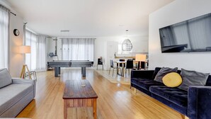 Ett modernt vardagsrum med ett soffbord i trä, en grå soffa, en mörkblå soffa med en gul kudde och en matplats i bakgrunden.