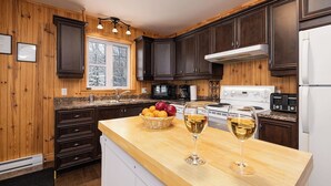 Una cocina con armarios de madera oscura, encimera de granito, refrigerador blanco y ventana con vista a árboles.